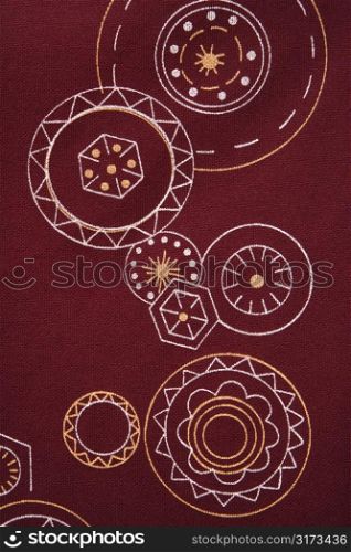 Close-up of maroon vintage fabric with white and yellow lines and shapes printed on polyester.