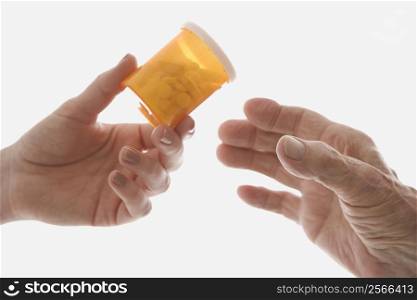 Close-up of mid-adult Caucasian female&acute;s hand handing medication bottle to elderly Caucasian male hand.