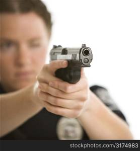Close up of mid adult female Caucasian law enforcement officer aiming gun at viewer with one eye closed.