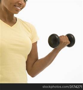 Close up of mid adult multiethnic woman wearing yellow exercise shirt doing arm curls looking at viewer and smiling.