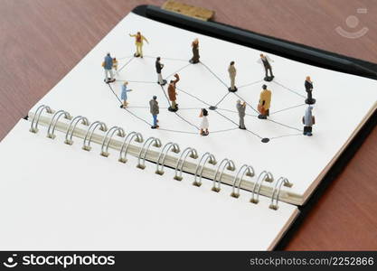 close up of miniature people with social network diagram on open notebook on wooden desk as social media concept