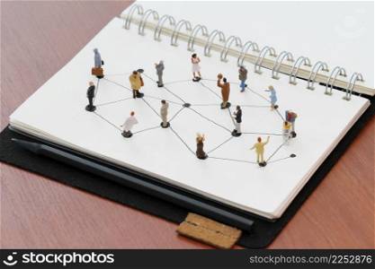 close up of miniature people with social network diagram on open notebook on wooden desk as social media concept
