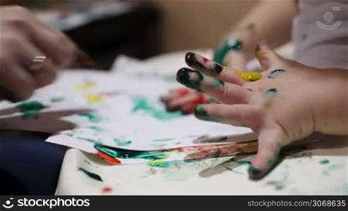 Close-up of mother&acute;s and her son&acute;s hands painting with colorful finger paints.