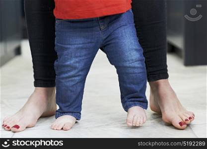 Close Up Of Mother Helping Baby Son To Walk In Kitchen