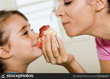 Close-up of mother sharing a pastry with her daughter