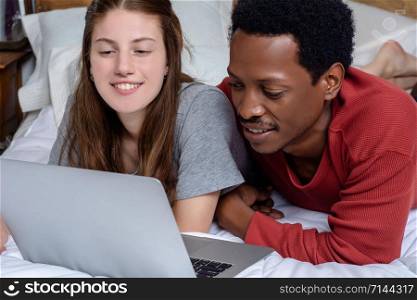 Close-up of Multiracial couple using laptop in a comfortable bed at home.