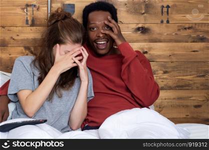 Close-up of Multiracial couple watching tv in a comfortable bed at home.