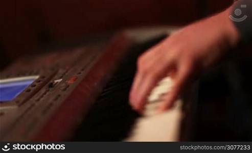 Close up of musiacian hands playing keyboard at the party in spotlights. Teenage pianist playing digital piano while rock band performing music on stage.