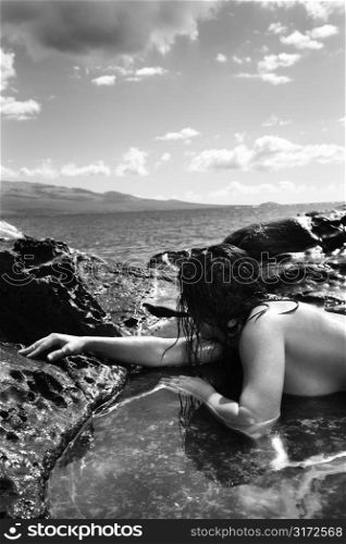 Close up of nude Caucasian mid adult woman lying in tidal pool at Maui coast looking toward ocean.