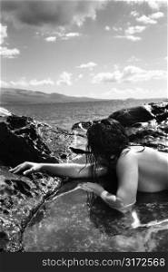 Close up of nude Caucasian mid adult woman lying in tidal pool at Maui coast looking toward ocean.