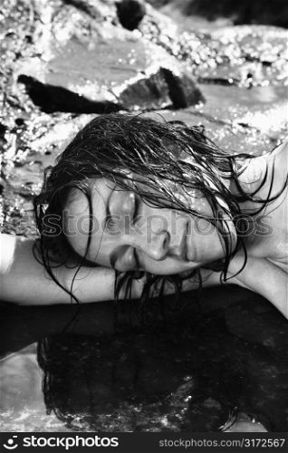 Close up of nude Caucasian mid adult woman lying in water at Maui coast with head resting on arm.