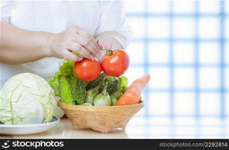 Close up of overweight woman hand preparing various organic vegetables into bamboo basket for cooking on kitchen table, healthy lifestyle concept