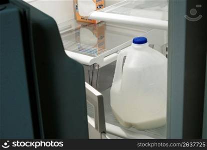 Close up of partial gallon of milk in otherwise empty refrigerator through open door