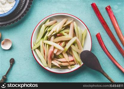 Close up of peeled and sliced rhubarb in bowl on kitchen table background, top view. Seasonal food concept. Rhubarb cake preparation.