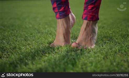 Close up of perfect woman&acute;s legs bare foot doing tiptoes yoga feet warm-up exercise on the green grass in the park
