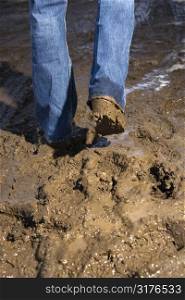 Close up of person walking in mud wearing jeans and boots.