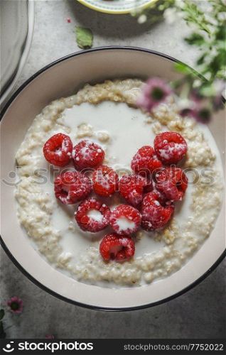 Close up of porridge bowl with heart of raspberries. Romantic breakfast with healthy ingredients. Heart shaped berry fruits. Top view.