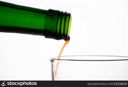 Close up of pouring fruit juice from green bottle into glass, isolated on white background.