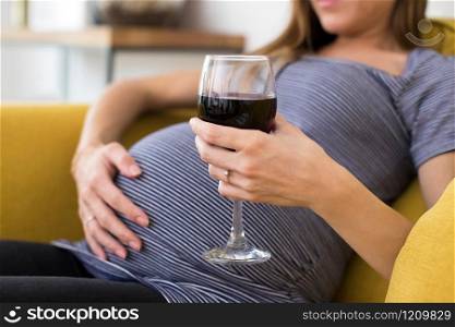 Close Up Of Pregnant Woman Drinking Red Wine Sitting On Sofa At Home