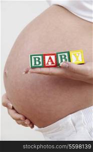Close Up Of Pregnant Woman Holding Blocks Spelling Baby