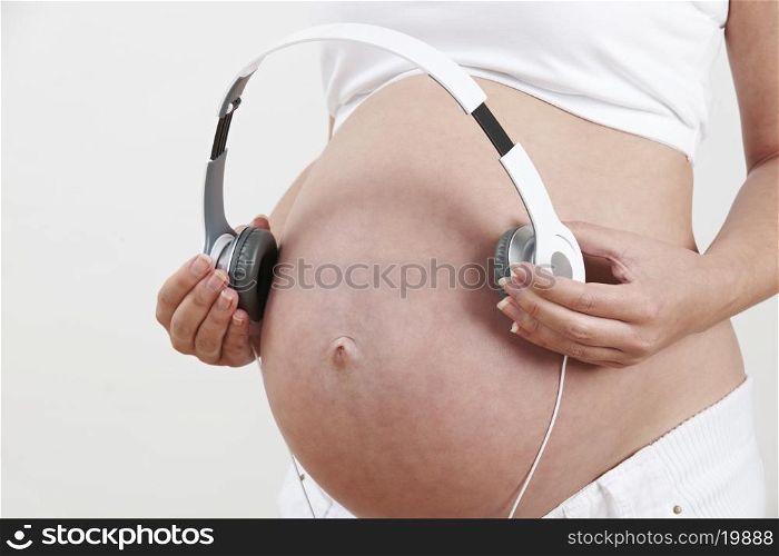 Close Up Of Pregnant Woman Holding Headphones Over Belly