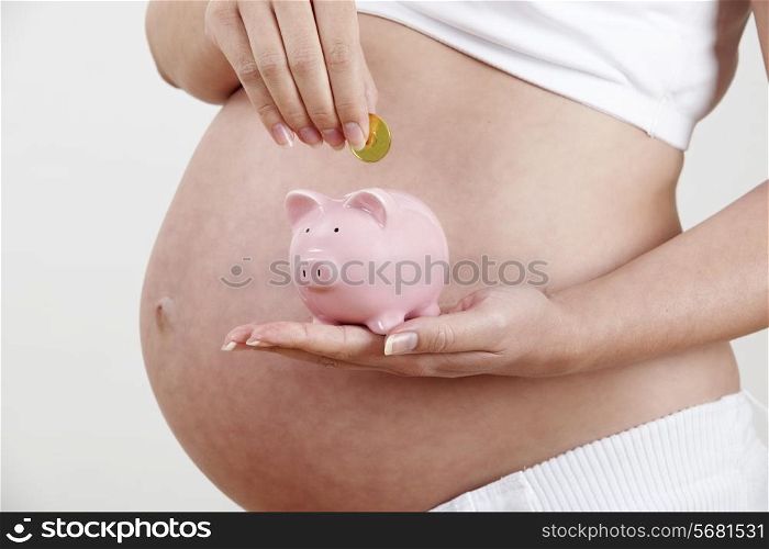 Close Up Of Pregnant Woman Putting Coin Into Piggy Bank
