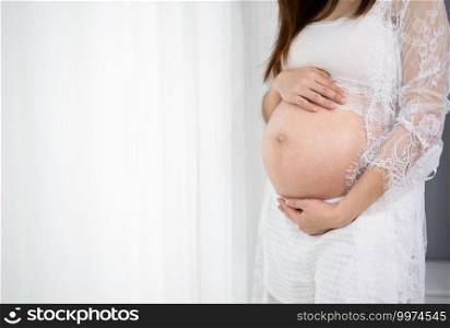 close up of pregnant woman stroking her belly on window background