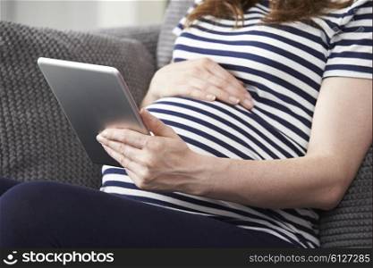 Close Up Of Pregnant Woman Using Digital Tablet At Home