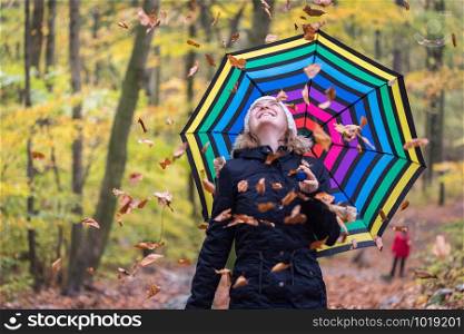 Close up of pretty young girl with a colorful umbrella in autumnal forest. Leaves are falling down.