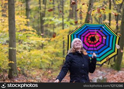 Close up of pretty young girl with a colorful umbrella in autumnal forest. Leaves are falling down.