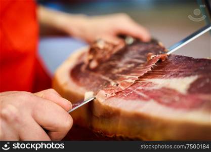 Close-up of professional cutter carving slices from a whole bone-in serrano ham. Professional cutter carving slices from a whole bone-in serrano ham