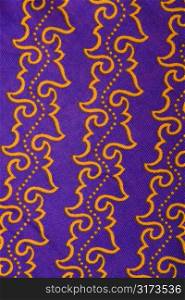 Close-up of purple vintage fabric with repetitive orange designs printed on polyester.