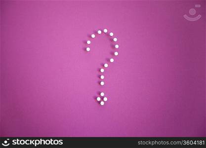 Close-up of push pins forming question mark over pink background