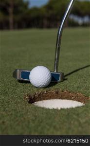 close up of putter hitting golf ball to hole at course