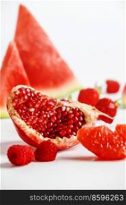 Close up of quarter of pomegranate, watermelon, raspberries and grapefruit at white background. Healthy  sweet red summer fruits for refreshing snack. Front view.