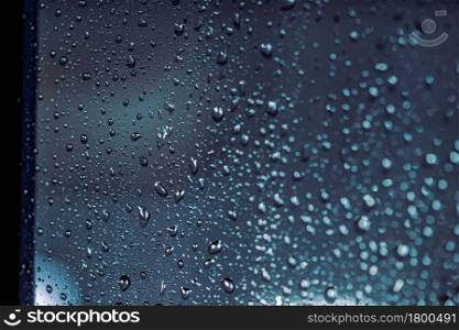 Close up of rain drops on the window in rainy night, cool lights and window frame