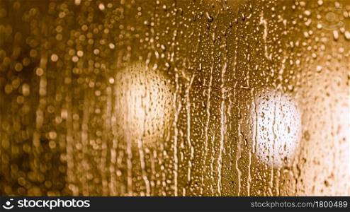Close up of rain drops on the window in rainy night, warm lights