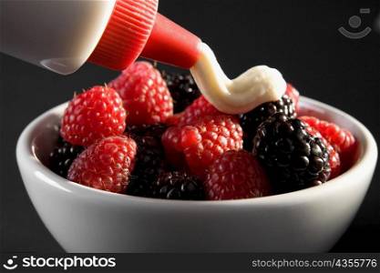 Close-up of raspberries and blackberries in a bowl with cream poured on top