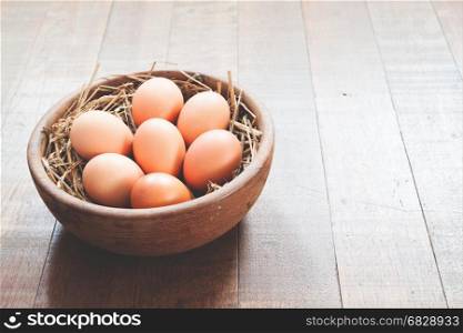 Close-up of raw chicken eggs in wooden bowl on wood background