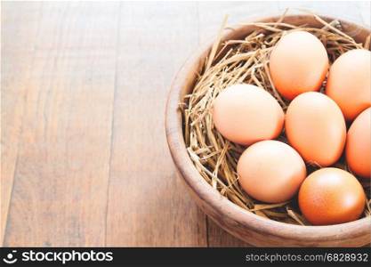 Close-up of raw chicken eggs in wooden bowl on wood background with copy space