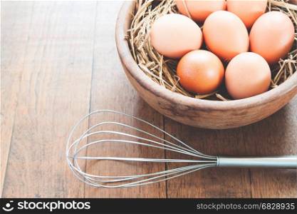 Close-up of raw chicken eggs in wooden bowl on wood background with kitchen utensil