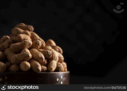 Close up of raw groundnuts kept in a wooden bowl on a black background. 