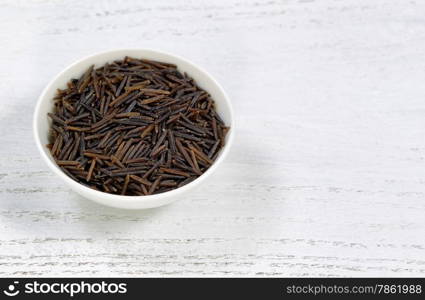 Close up of raw wild rice in bowl on white wood.