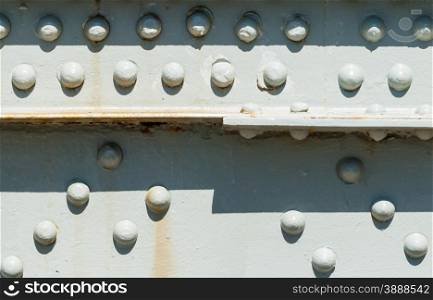 Close-up of rivets on painted steel surface with some rust stains, partly casting shadows from top.