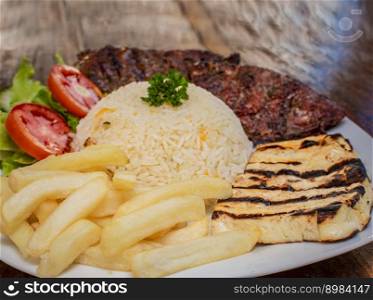 Close-up of roast beef with tomato salad and french fries, traditional barbecue roast beef food served on wooden table, plate with roast beef and salad served on wooden background