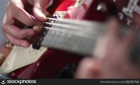 Close up of rock musician hand strumming at electric guitar strings. Man playing electric guitar with different techniques, bending and tapping while recording a brand new song in studio.