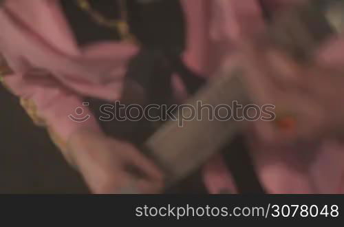 Close-up of rock musician hands playing electric bass guitar on stage. Midsection of musician playing bass guitar during band performing song.