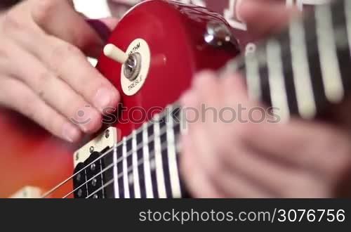 Close up of rock musician with electric guitar switching a guitar pickup selector from rhythm to treble and fretting chord. Guitarist playing on electric guitar with focus on hand fretting strings and fretboard.