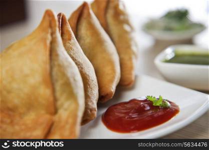 Close-up of samosas with tomato sauce and chutney in plate