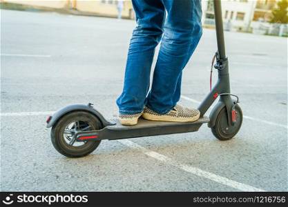 close up of senior man legs in jeans riding electric kick scooter on the yard asphalt in summer day in front of the building
